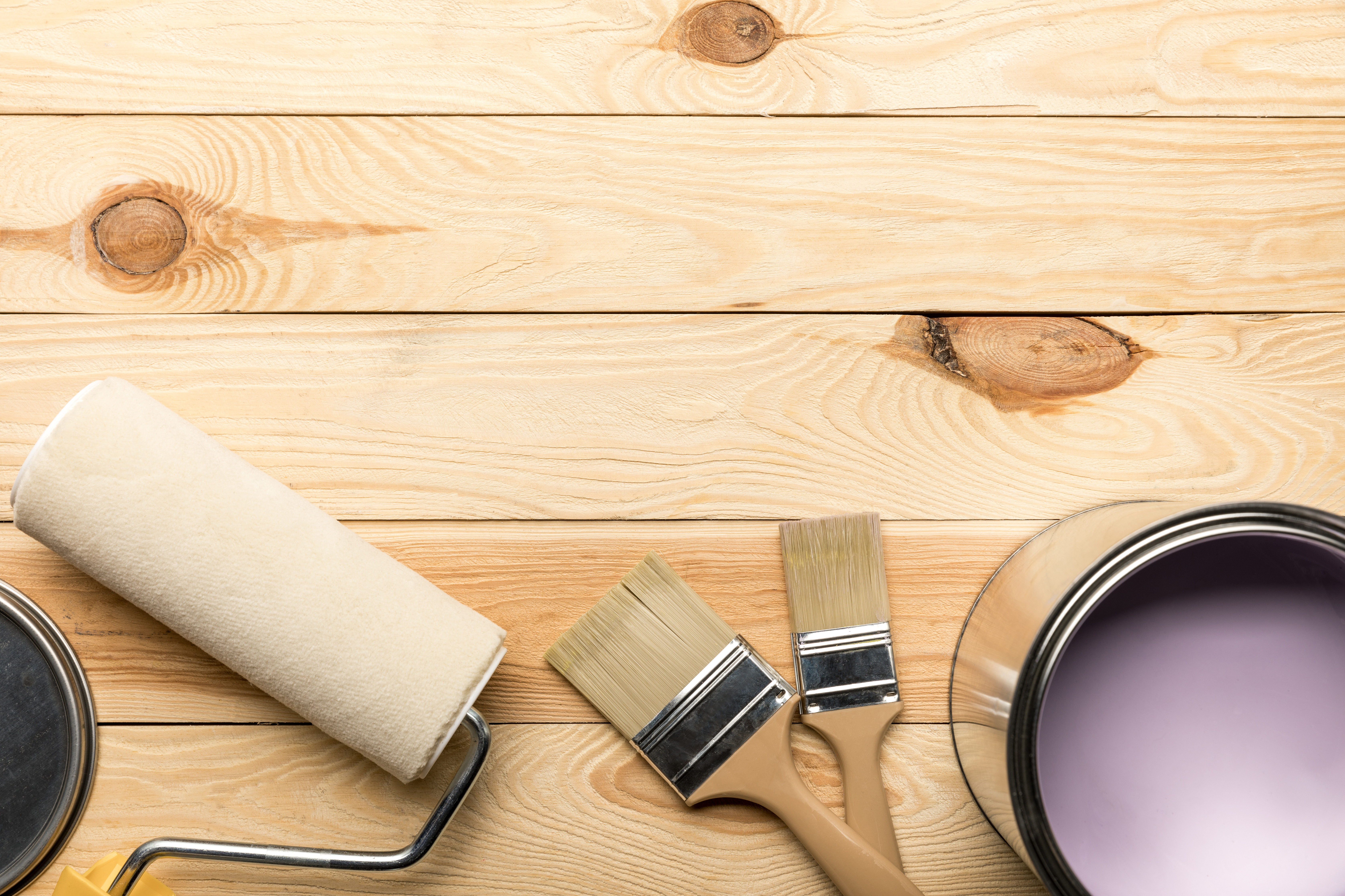 top view of brushes, tin of purple paint and paint roller on wooden surface