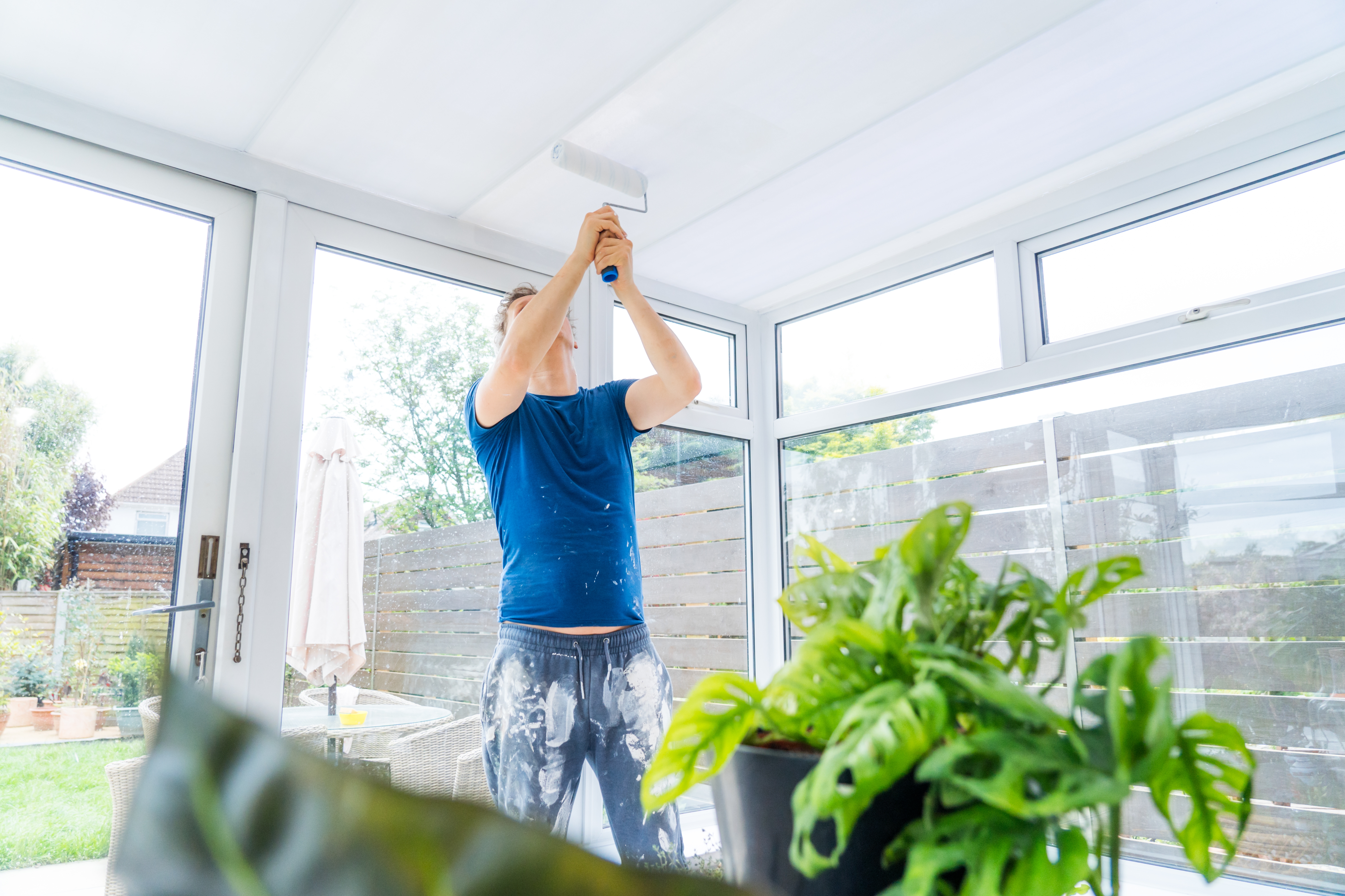 Young man painting the plastic ceiling of the conservatory in white color by the roller. DIY