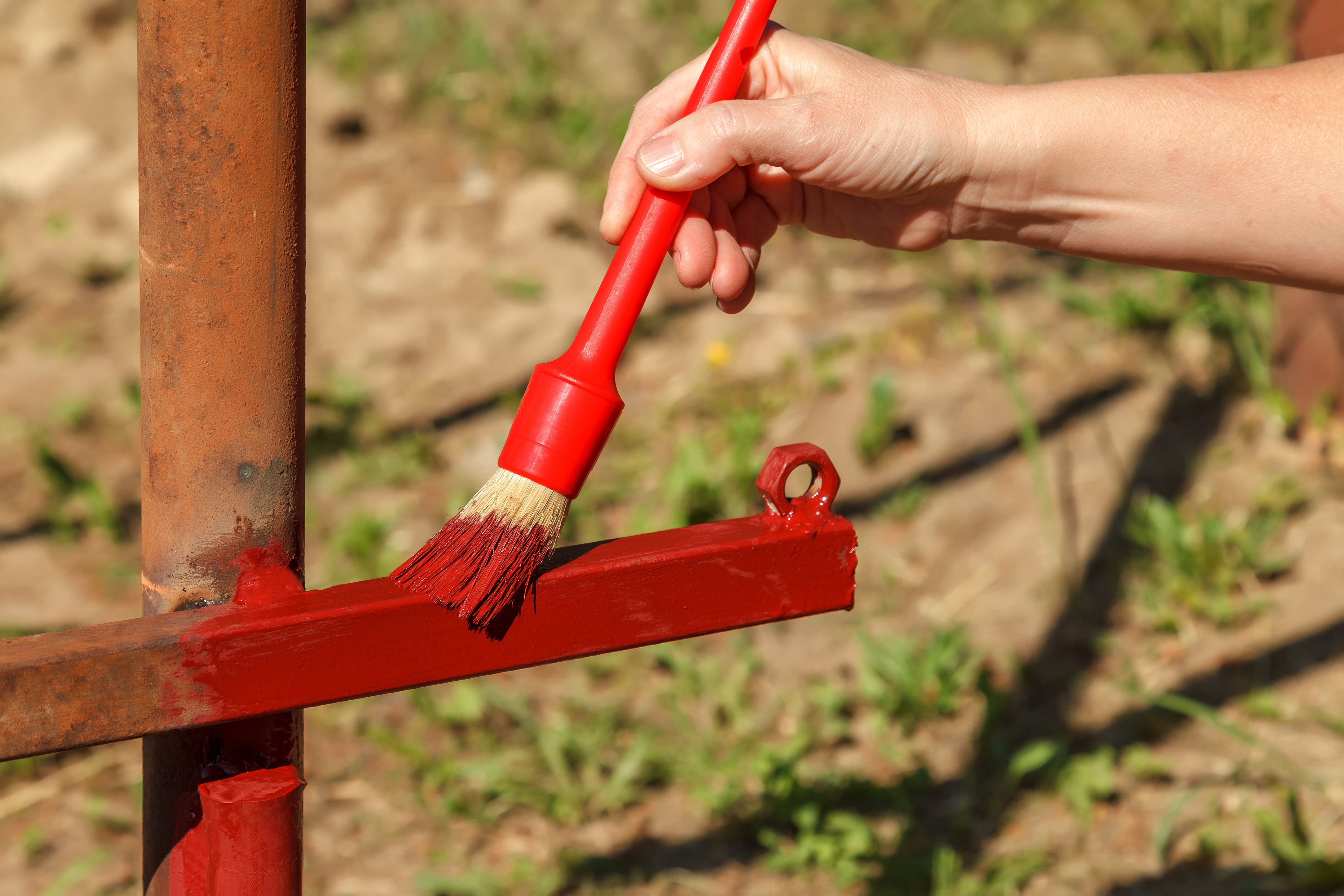 Young woman paints red primer metal structure